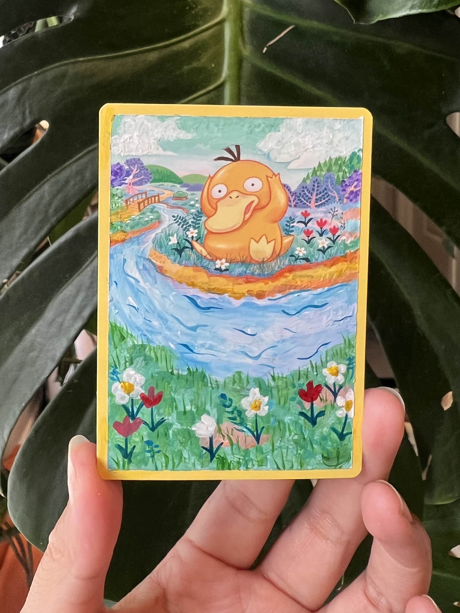 Card with a cartoon character in a boat held by a hand against a leafy background